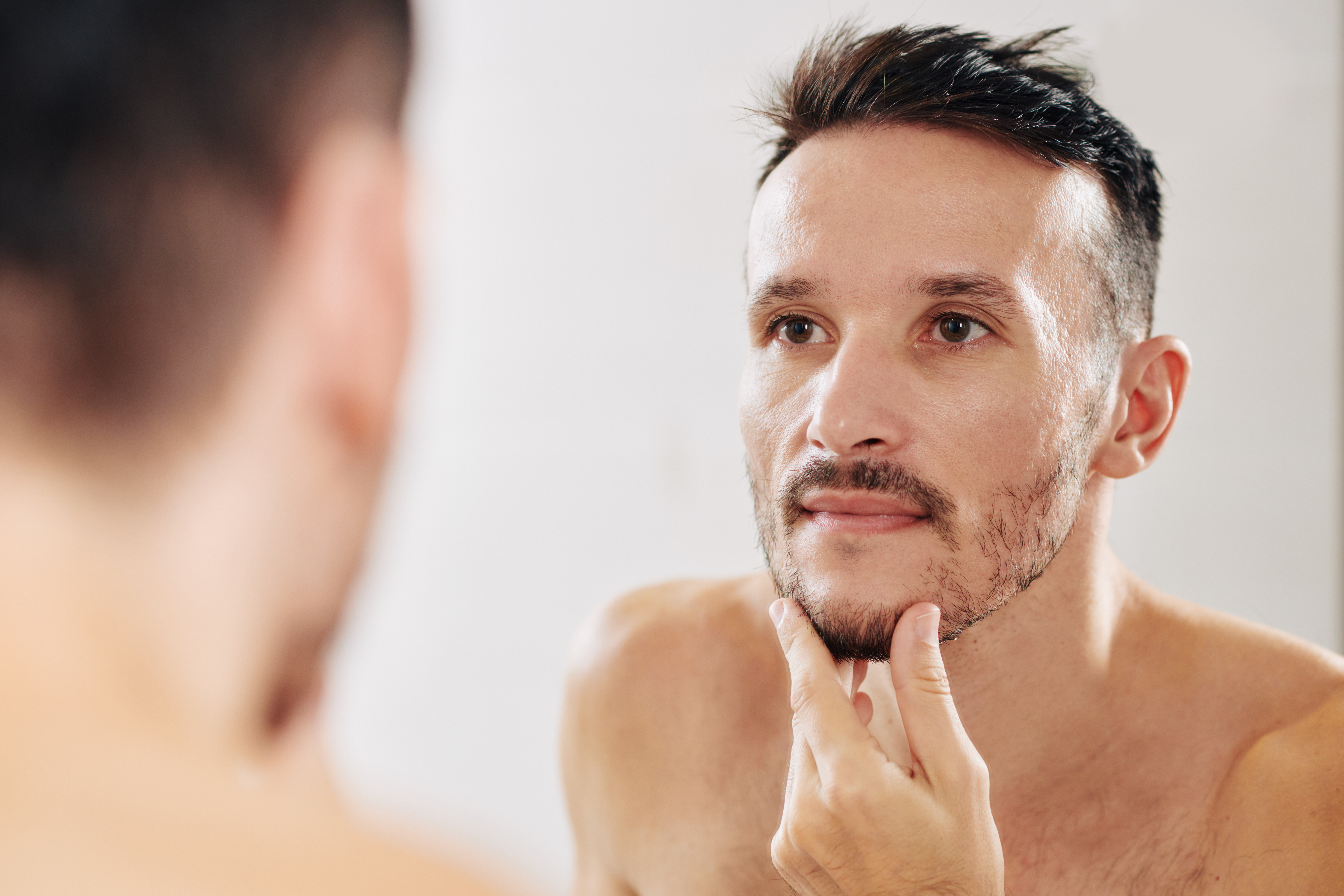 A Handsome Man stokes his refined chin in a mirror